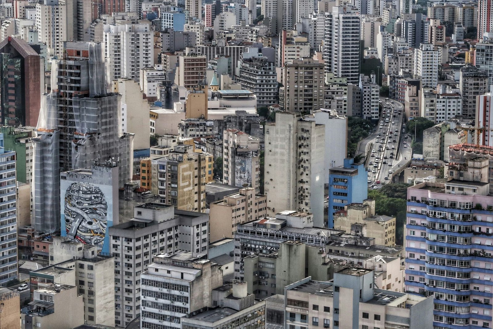 Mid-rise and high-rise buildings fill the whole frame, with a large mural on one side wall