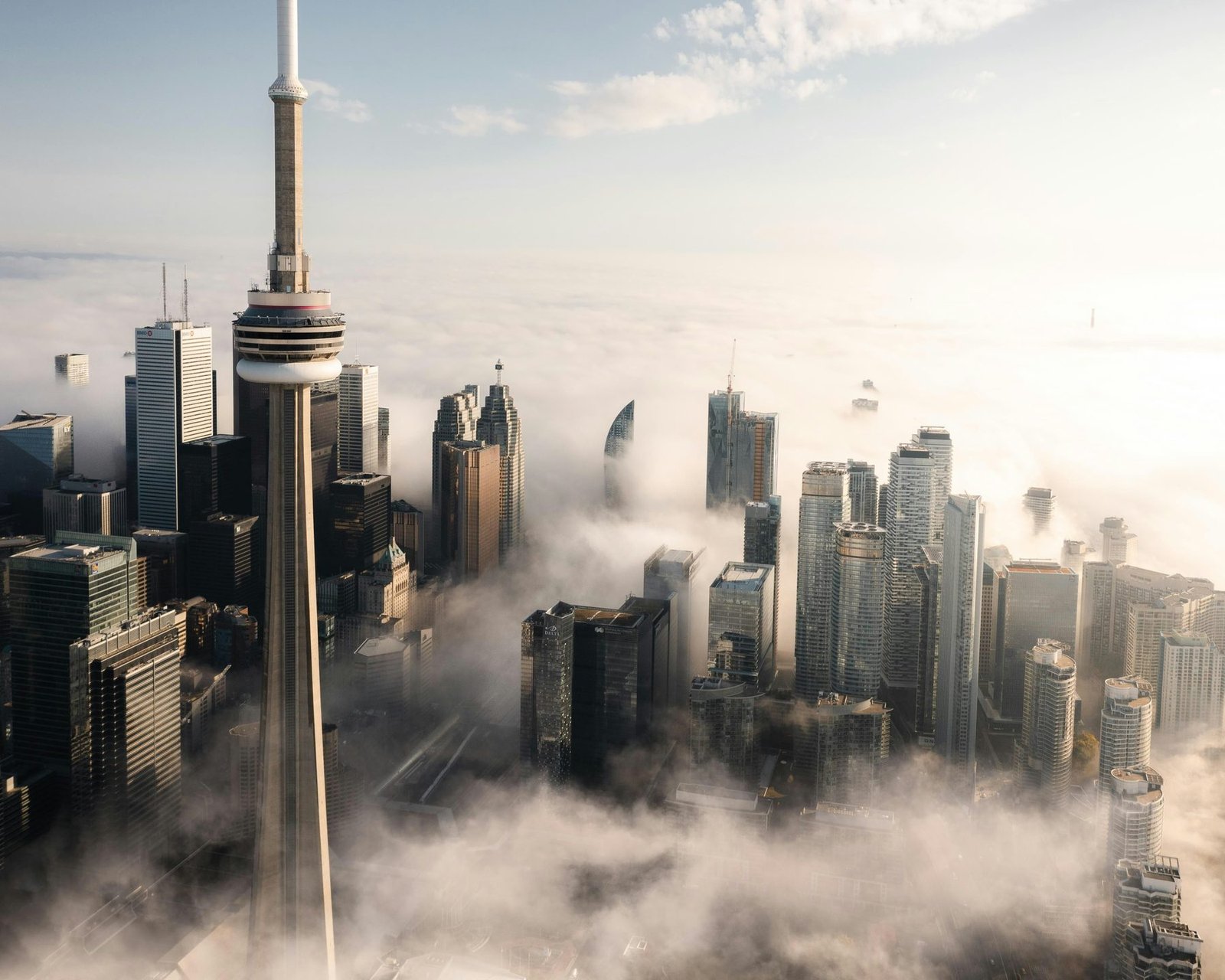 A tall concrete tower and the tops of skyscrapers rise out of a layer of fog in warm light