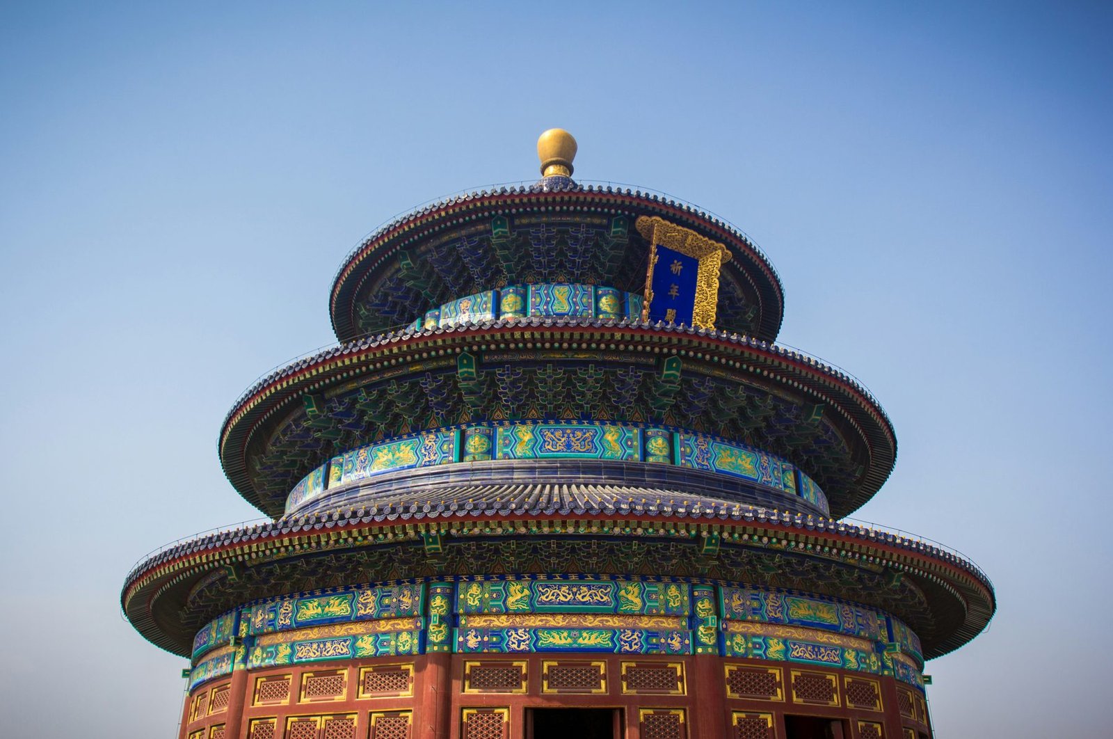 Three tiers of blue tiled circular roofs with painted eaves and a gilded finial rise against a clear blue sky