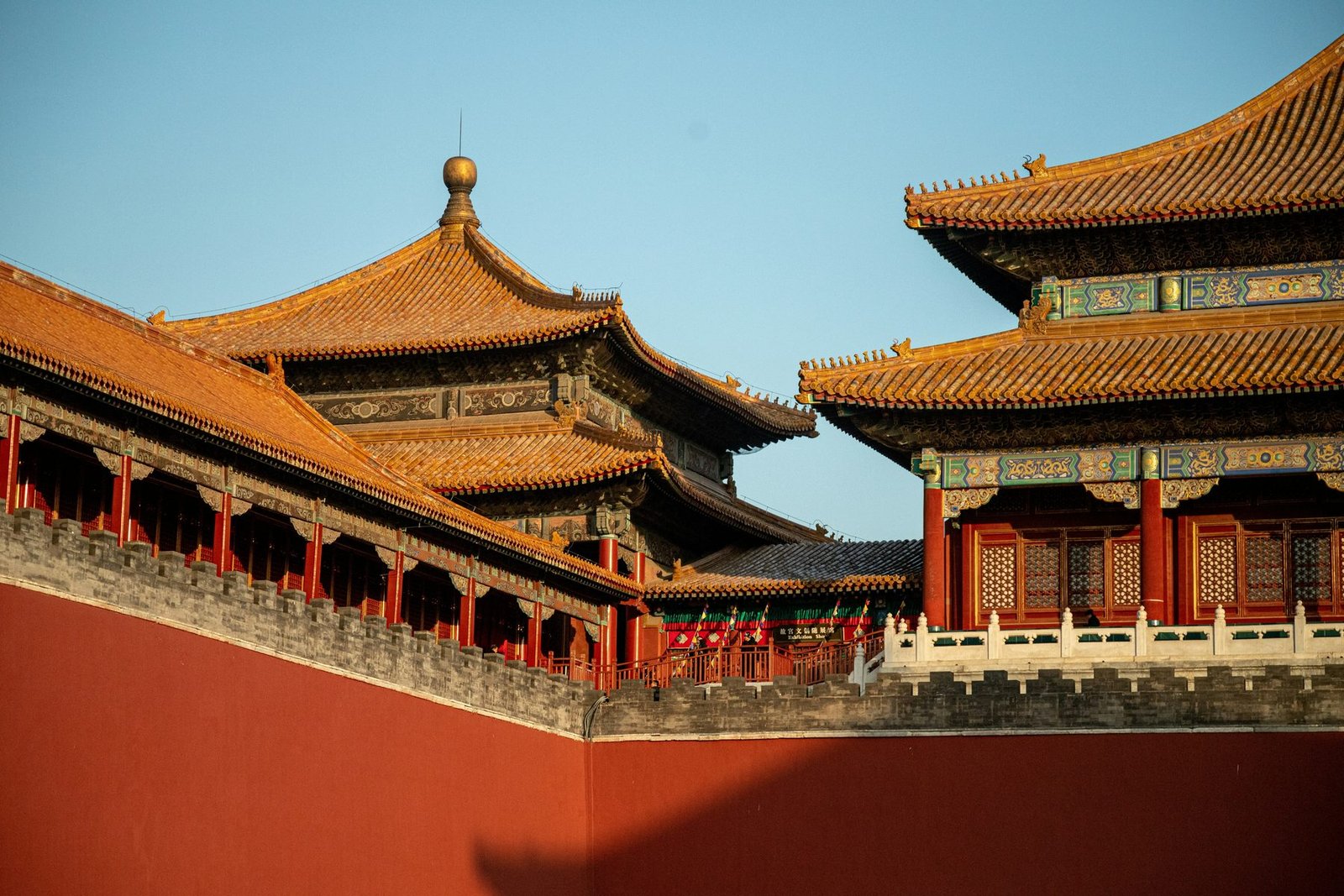 Layered yellow tiled roofs with painted eaves rise above a plain deep red wall under a clear blue sky