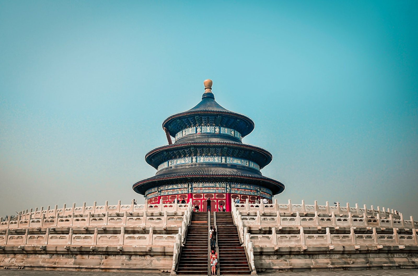 A round blue-roofed temple hall stands on tiered white marble terraces under a turquoise sky