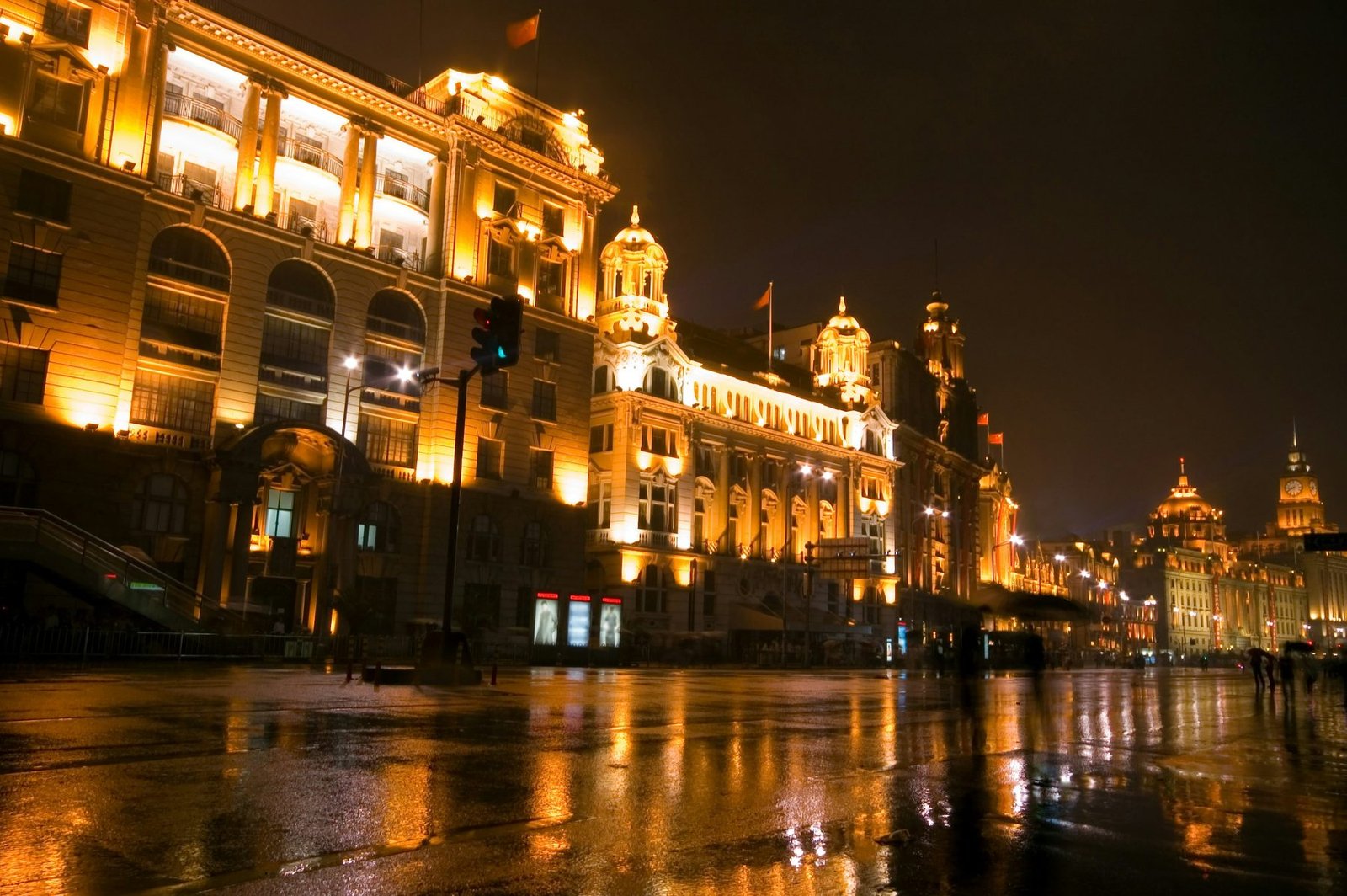 A row of floodlit stone buildings glows gold above wet pavement that mirrors the lights