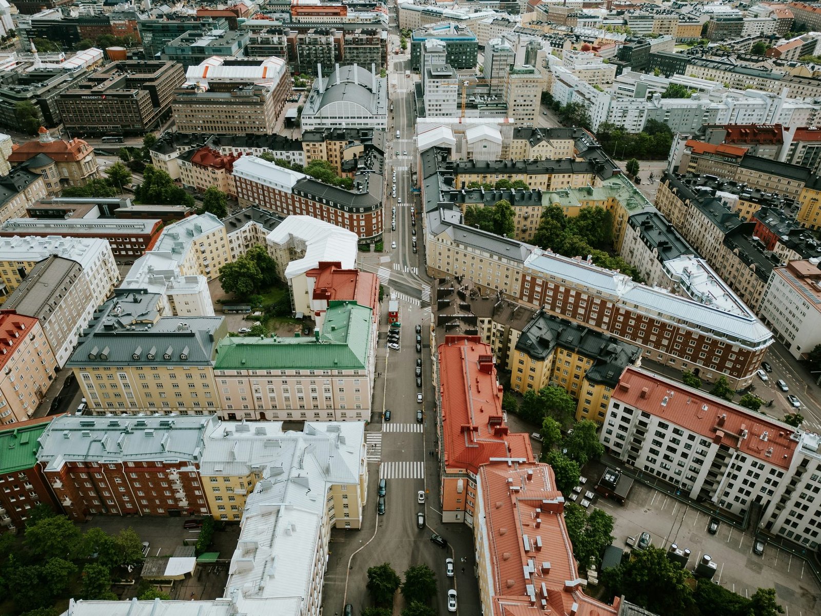 Blocks of apartment buildings with green, red and gray roofs are divided by straight streets, seen from the air