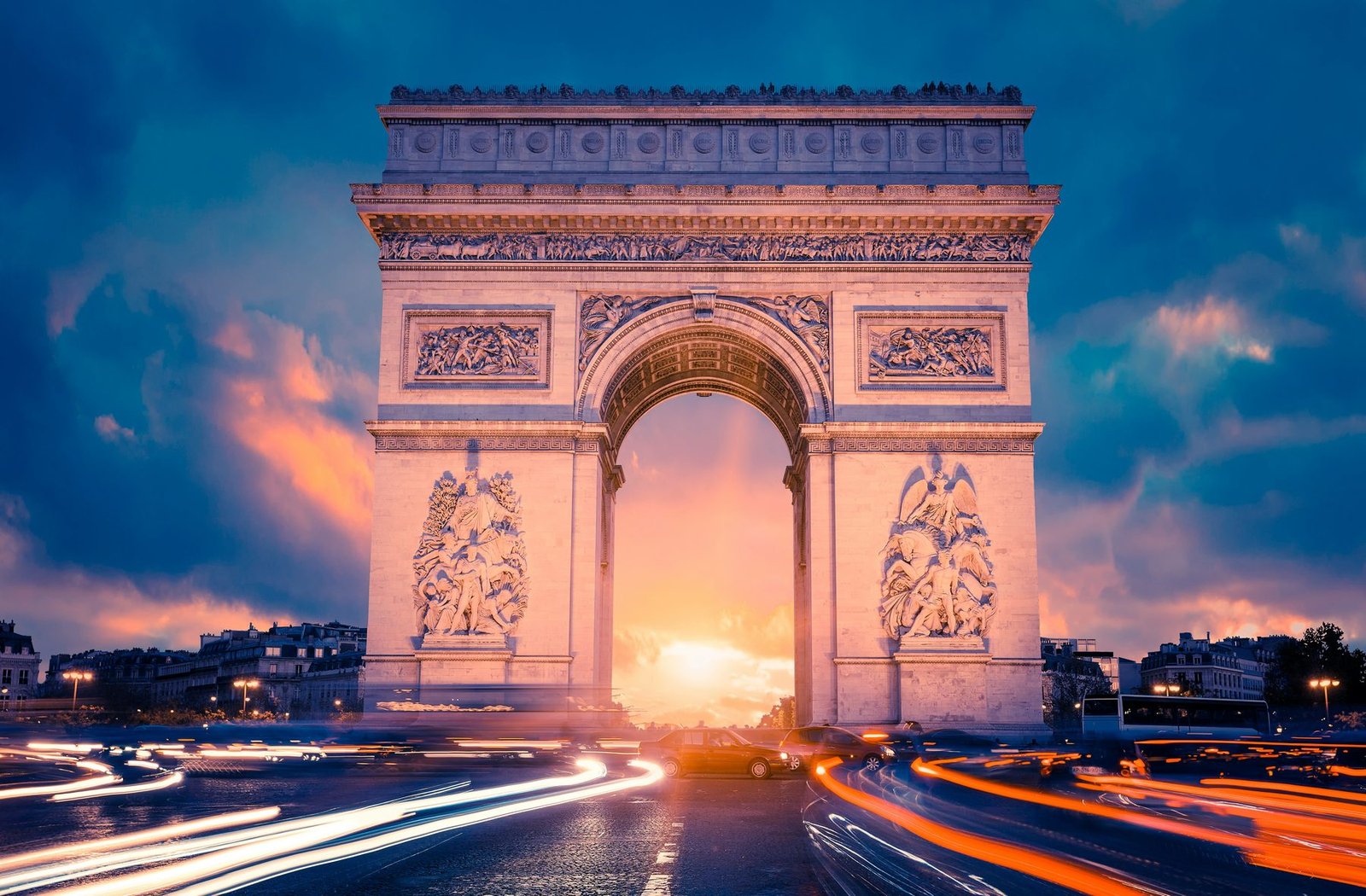 A large stone triumphal arch with the setting sun in its opening and streaks of traffic light around it