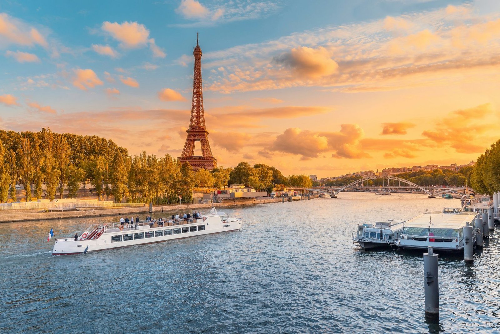The Eiffel Tower over the Seine at sunset, with a tour boat on the water