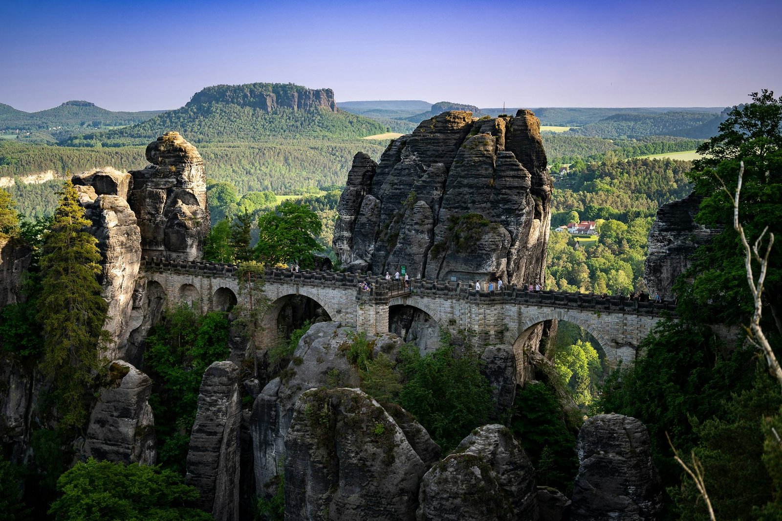 A stone bridge spans a gap between sandstone pinnacles, with a flat-topped hill on the horizon