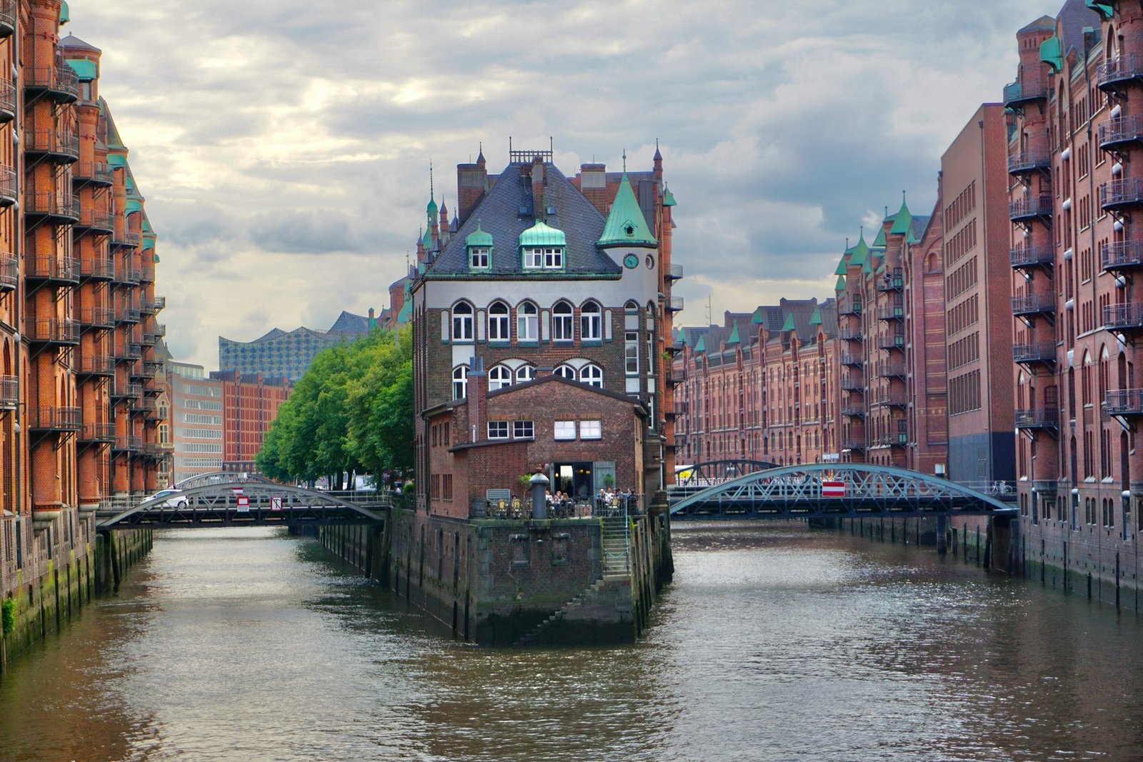 Red-brick warehouses line a canal, with a turreted brick building on a point between two iron bridges