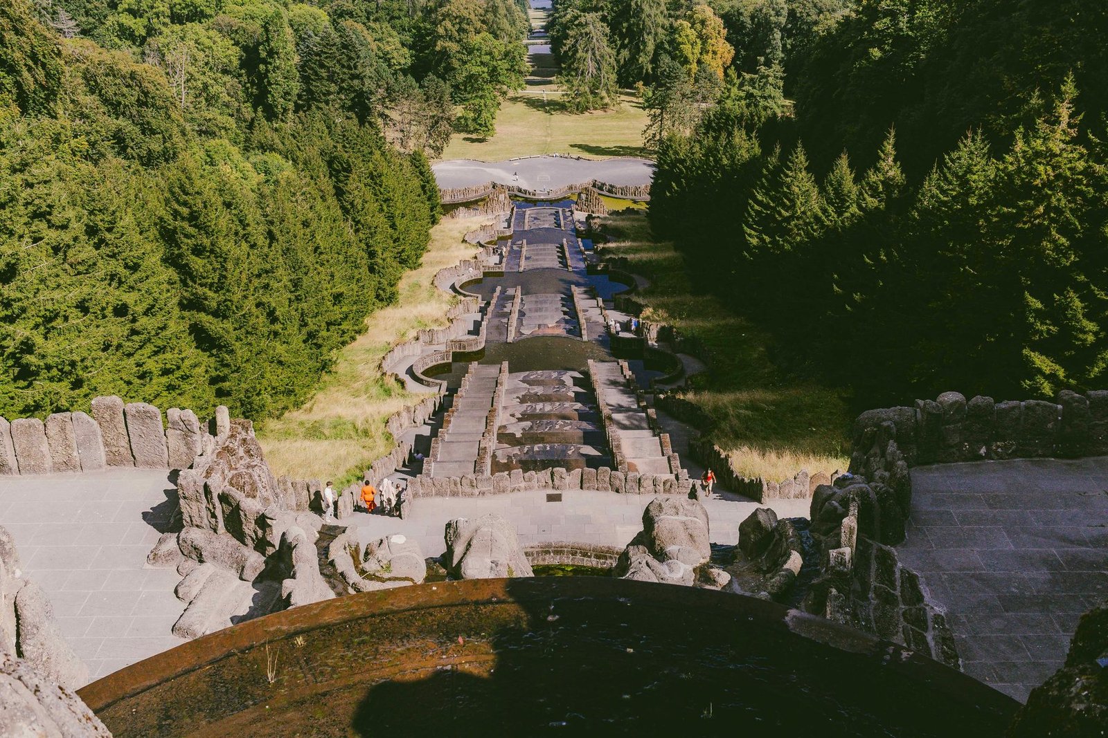 A long stepped stone cascade runs downhill between tall conifers, seen from above