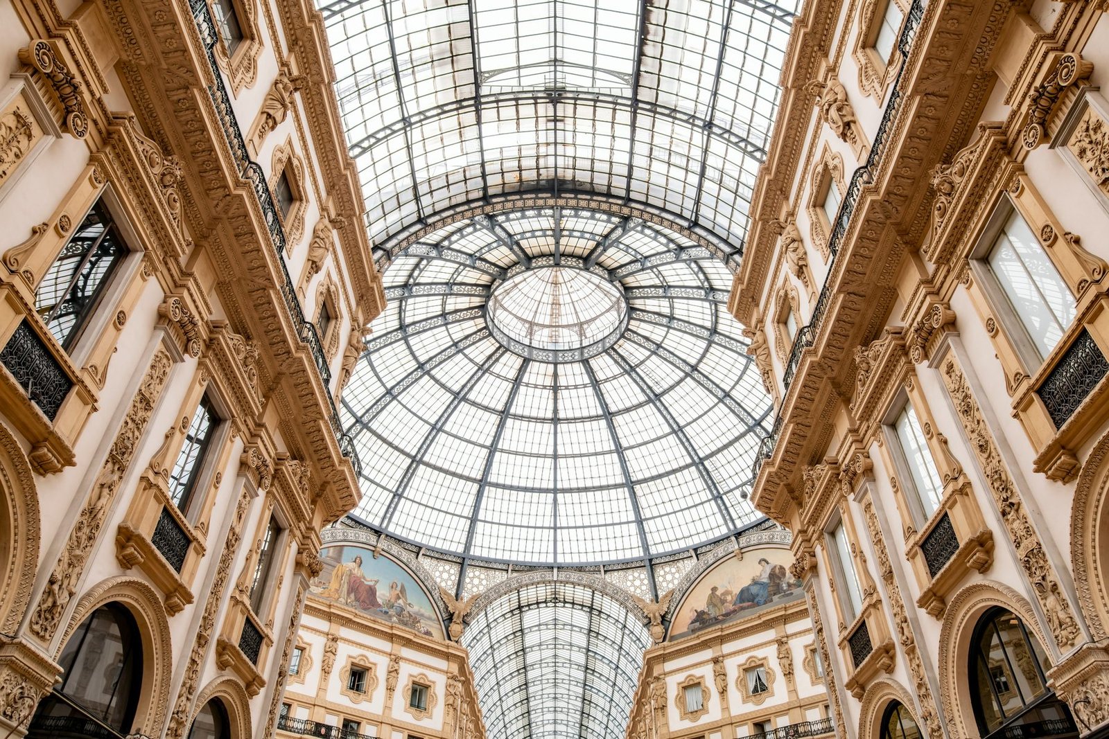 Tall ornate facades converge on a circular glass dome seen from directly below