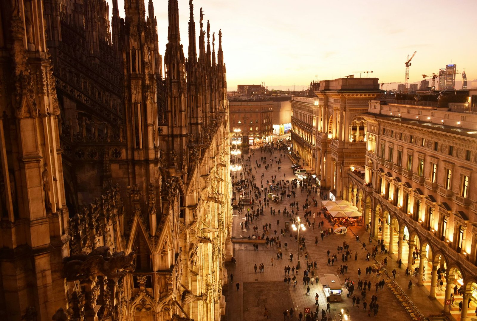 Gothic buttresses in warm light frame a crowded square and arcaded buildings below