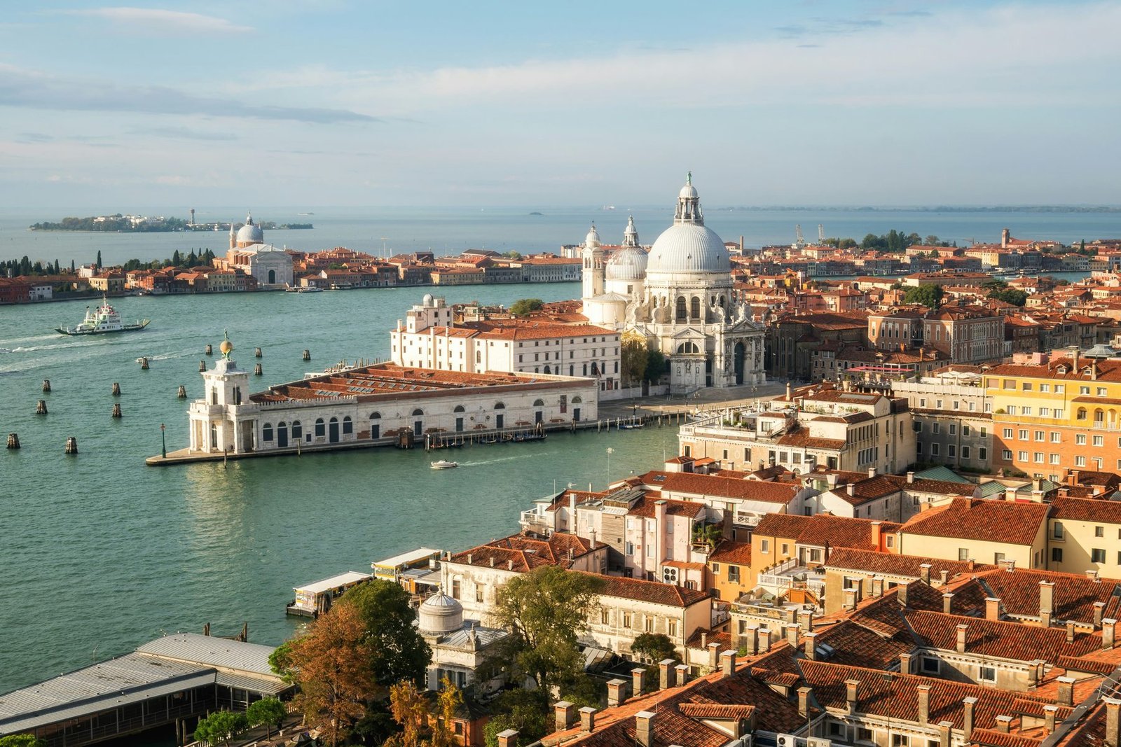 A high view over tiled roofs to a triangular point of land with a low customs house and a domed church, with the lagoon beyond