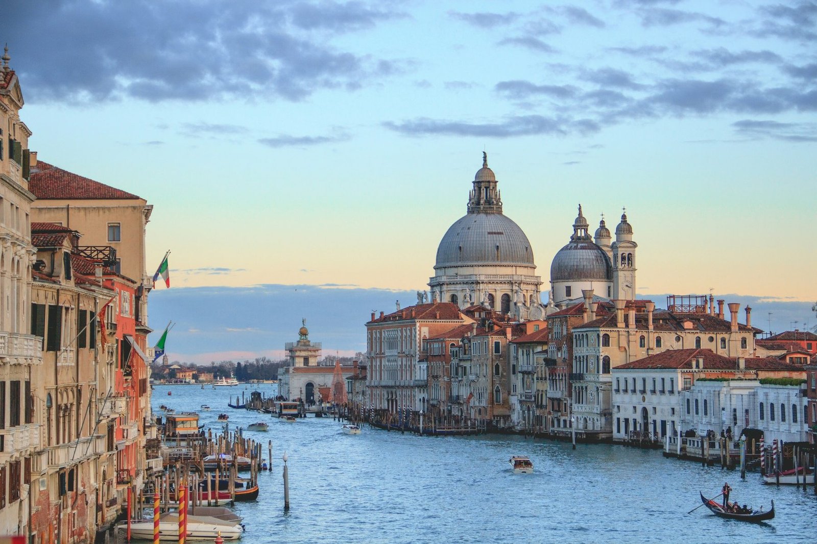 A large domed church stands at the mouth of a canal under blue-gray clouds, with palaces at left and a gondola on the water