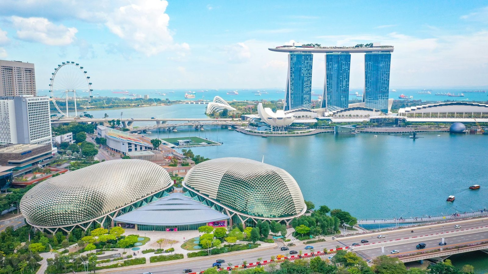 Two spiky domed halls sit on the edge of a blue bay facing a three-tower hotel, a white lotus-shaped museum and an observation wheel