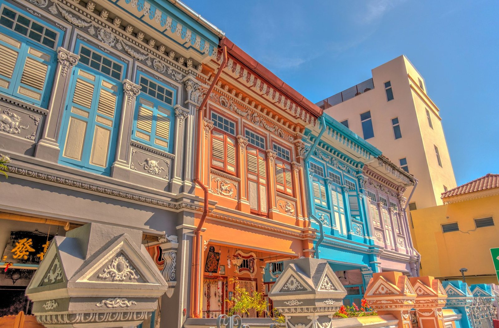 Looking up at two-story terrace houses painted blue, orange and turquoise with shuttered windows and molded plasterwork