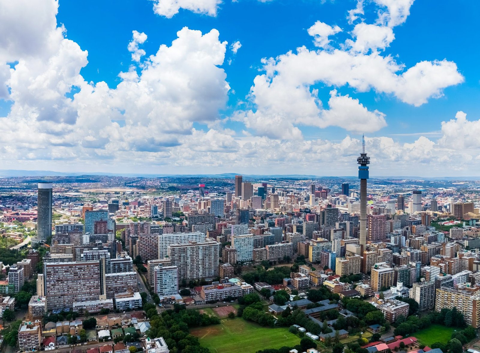 A tall telecom tower rises over apartment blocks beneath large white clouds