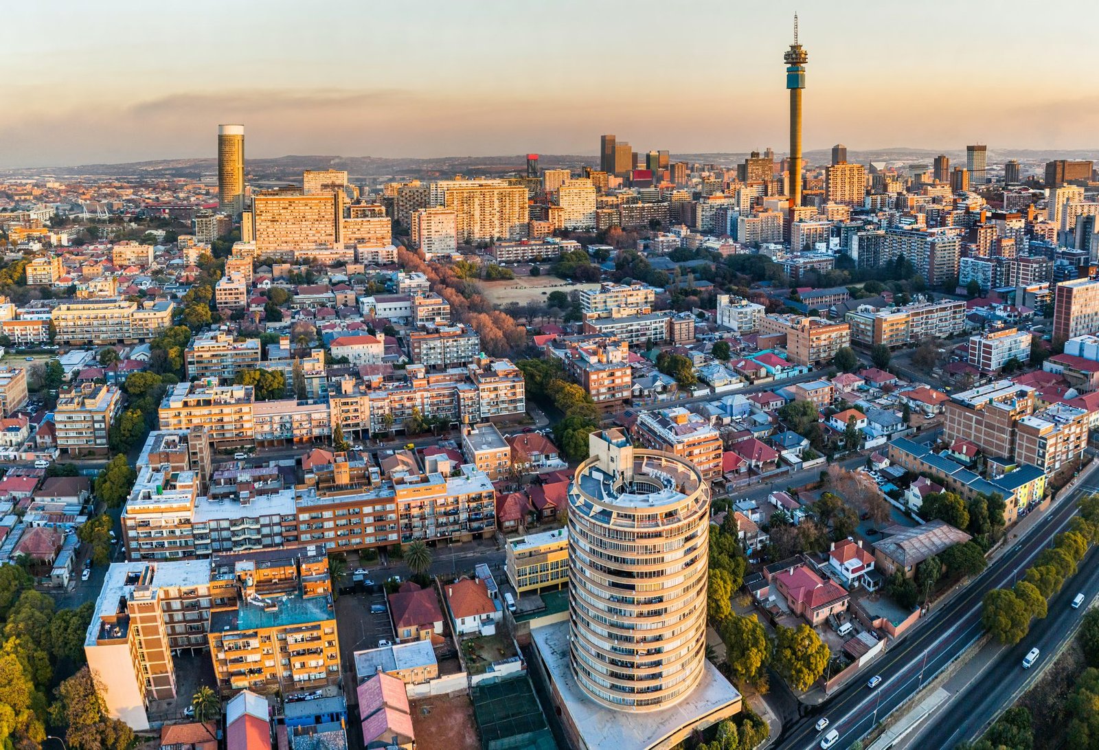 A cylindrical apartment tower stands in the foreground of a dense city with a tall telecom tower behind