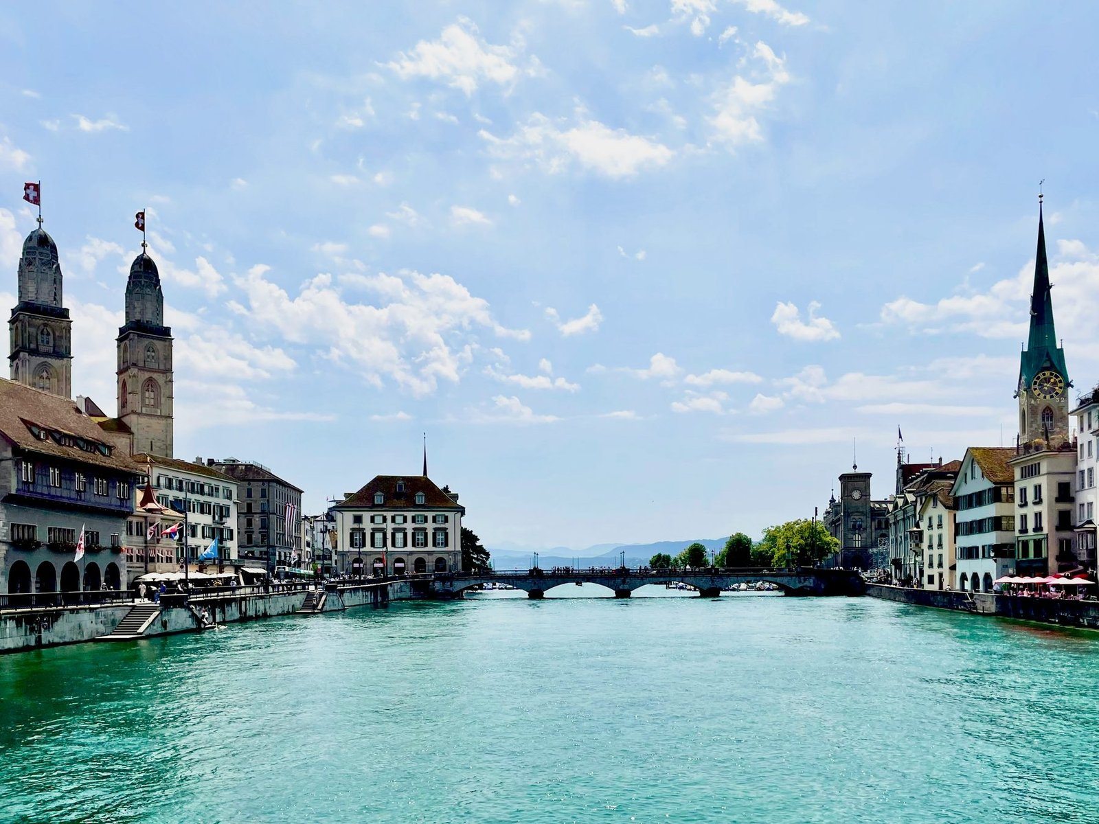 A turquoise river runs between old buildings and church spires toward a bridge