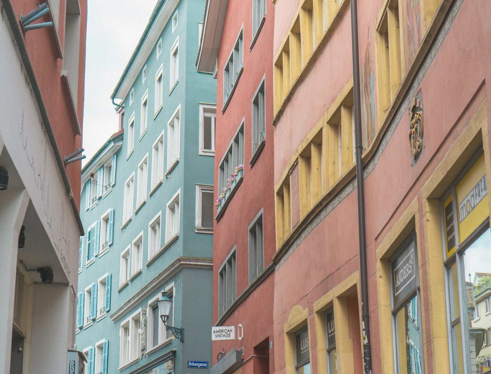 A view up a narrow lane at tall house fronts painted blue, pink and yellow with rows of shuttered windows