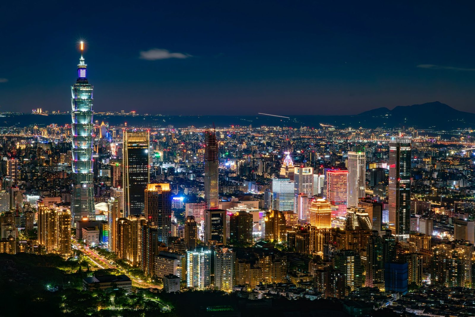 A tall tiered tower rises at the left over a wide basin of brightly lit buildings, with dark hills on the horizon