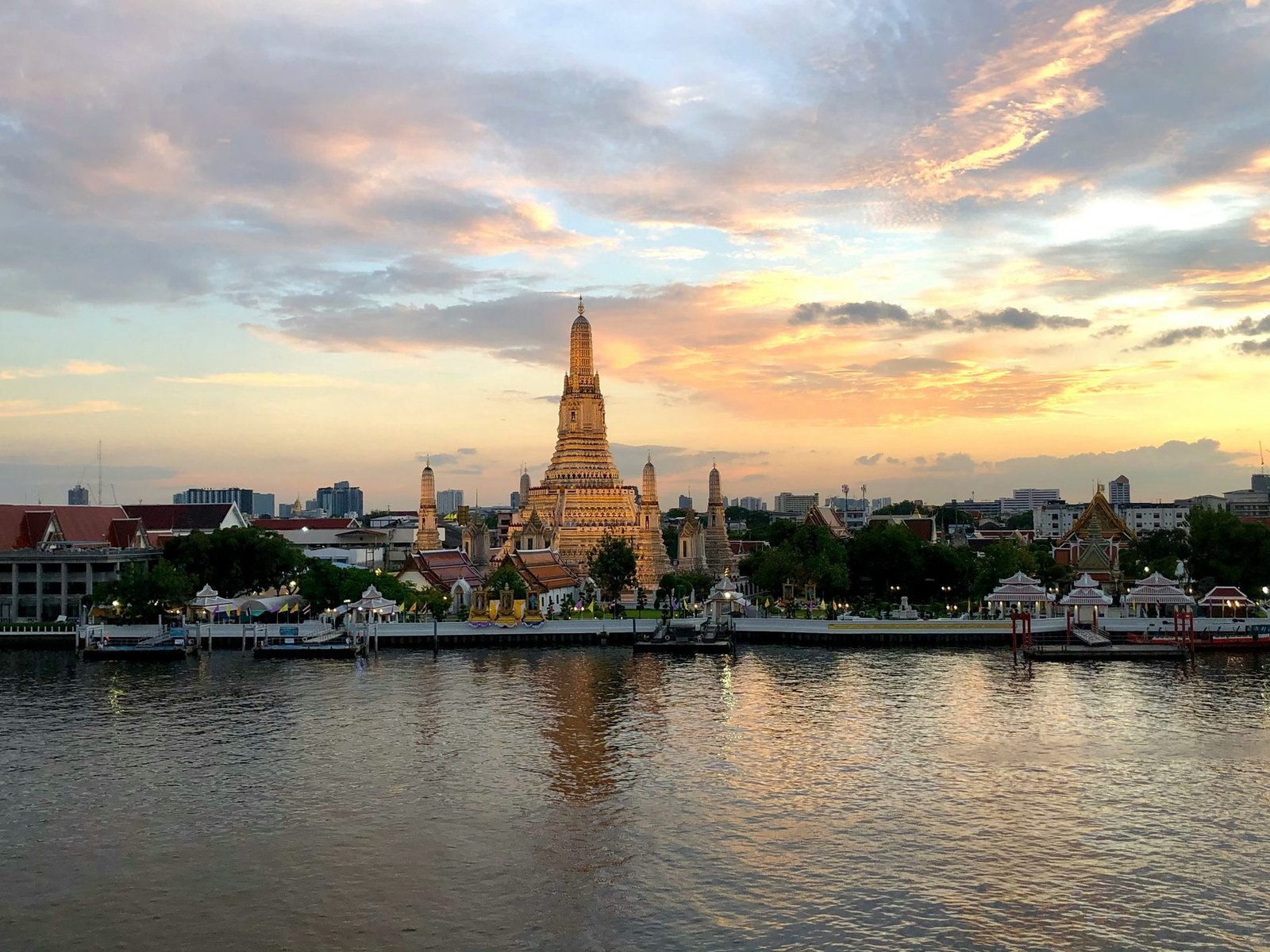 A temple spire stands on the far bank of a wide river under a sky of gray and orange cloud reflected in the water