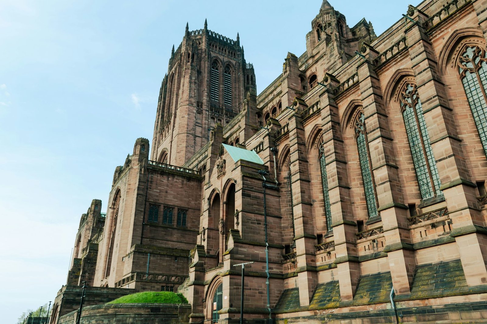 The red sandstone walls, buttresses and central tower of a very large Gothic cathedral seen at a steep angle