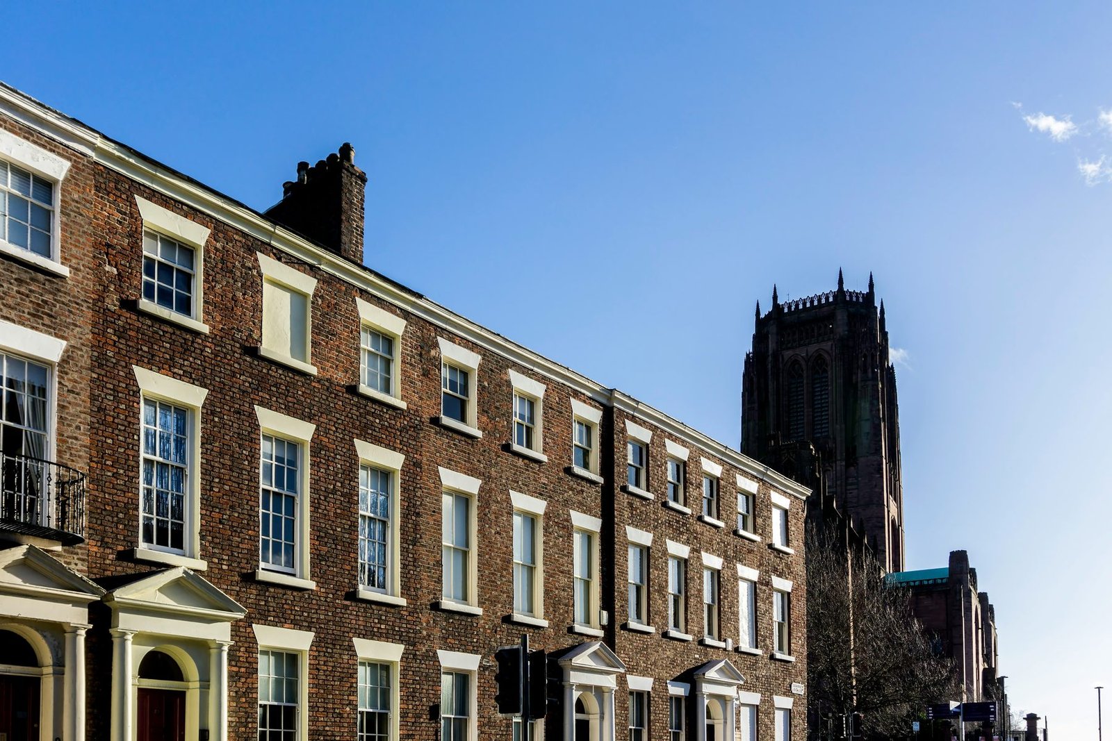 A row of brick terraced houses with white-framed sash windows, with a massive dark stone church tower behind against a blue sky