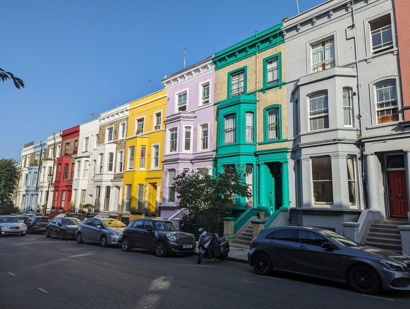A curving row of tall stucco houses painted white, red, yellow, lilac and green, with cars parked along the street