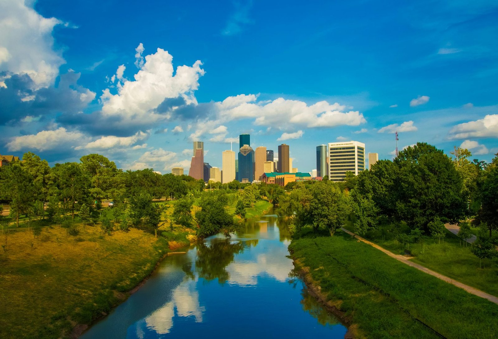 Clouds are reflected in a still stream between grassy banks, with small towers on the horizon