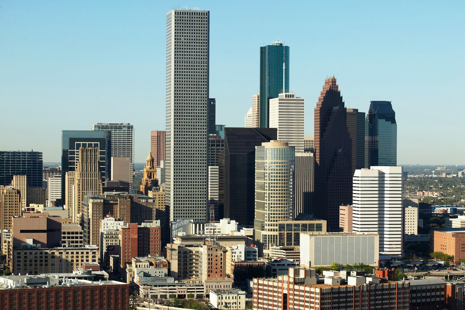 A tight group of skyscrapers in glass, granite and concrete stands above lower blocks under a clear sky
